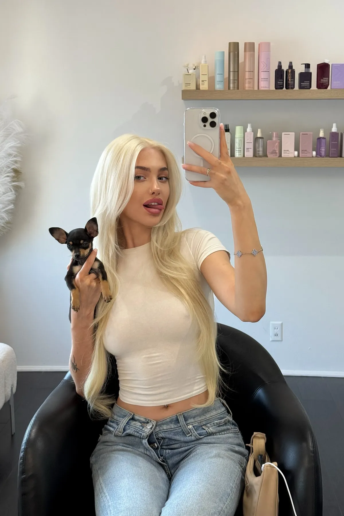 Alexandra Marianna taking a mirror selfie in a salon chair, holding a small black-and-tan dog