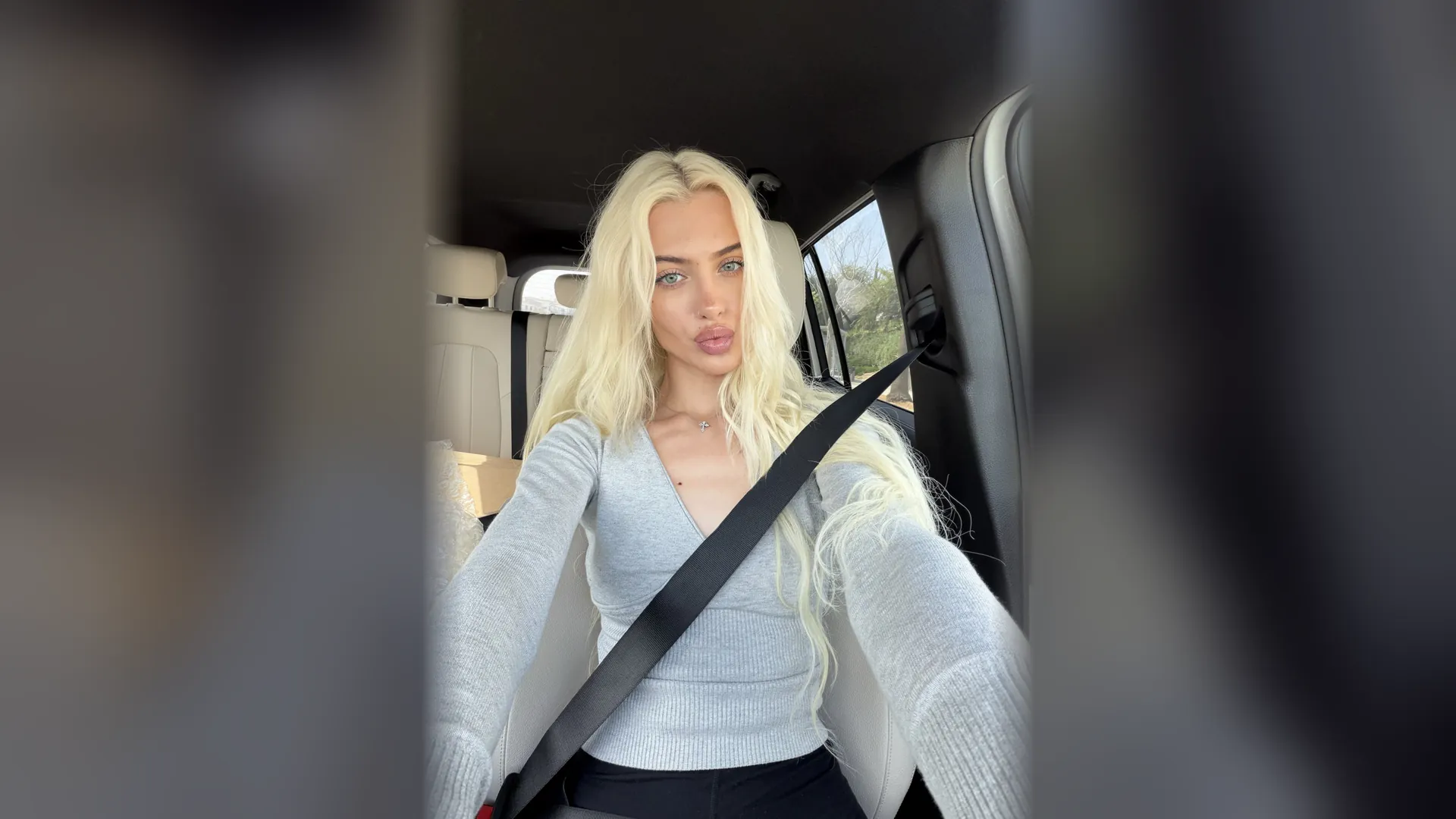 Alexandra Marianna taking a selfie in a car, wearing a pale blue cardigan