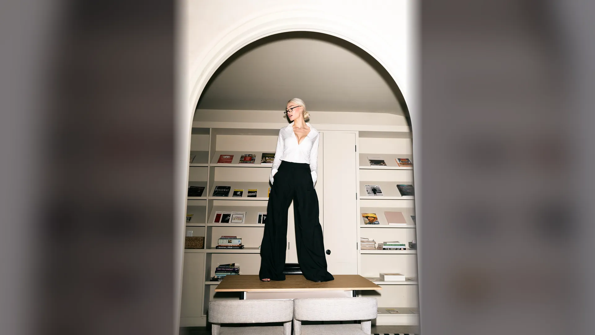 Alexandra Marianna in a white shirt in an arched doorway lined with bookshelves