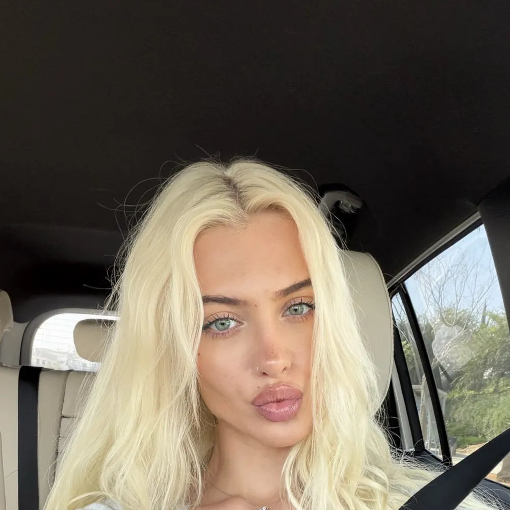 Alexandra Marianna taking a selfie in a car, in a pale blue cardigan